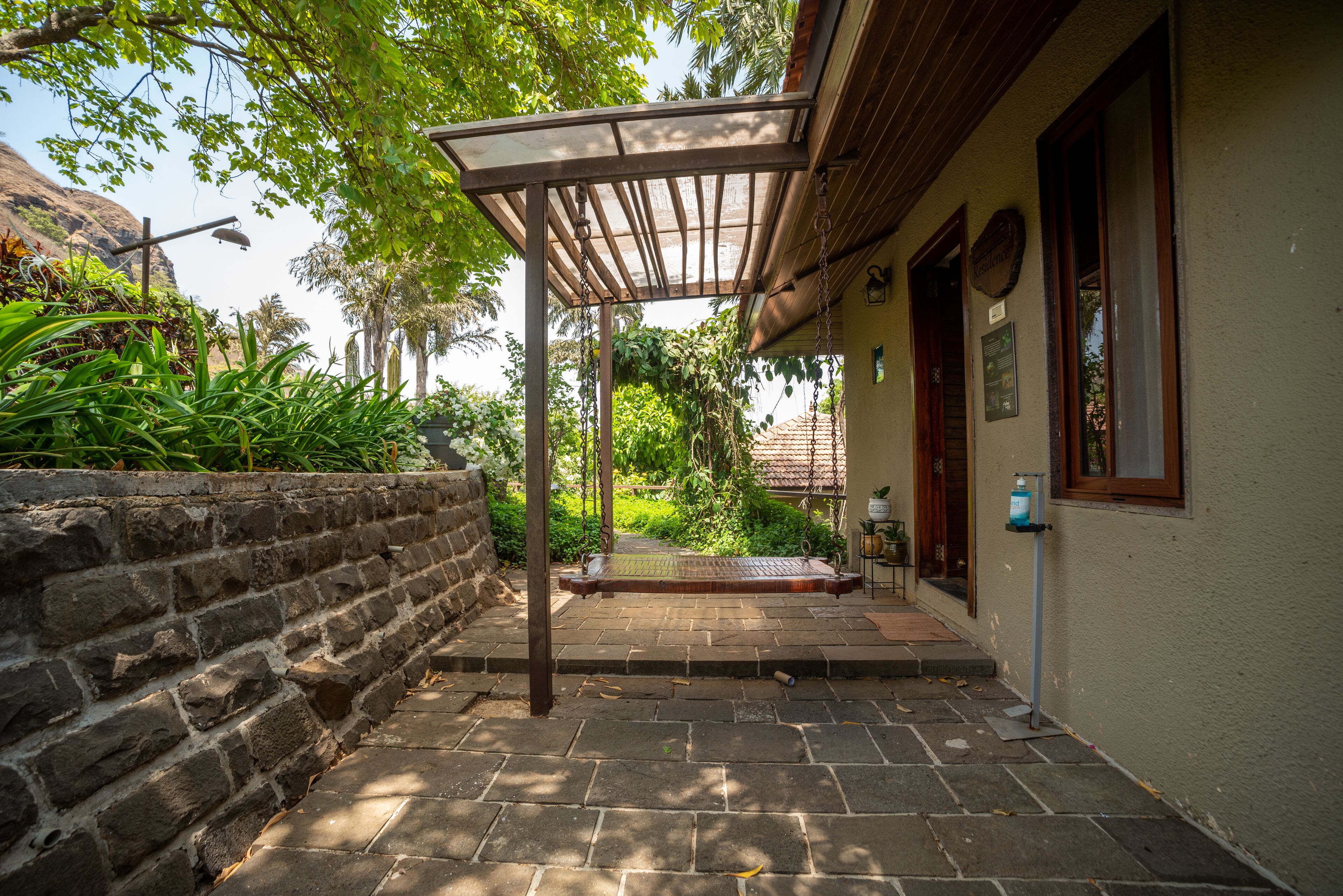 A covered outdoor area with a swing, a stone wall, and a building with a tiled roof.