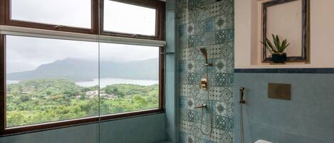 Un baño con una ventana grande, una ducha con pared de azulejos decorativos, un inodoro y una pequeña planta en maceta.