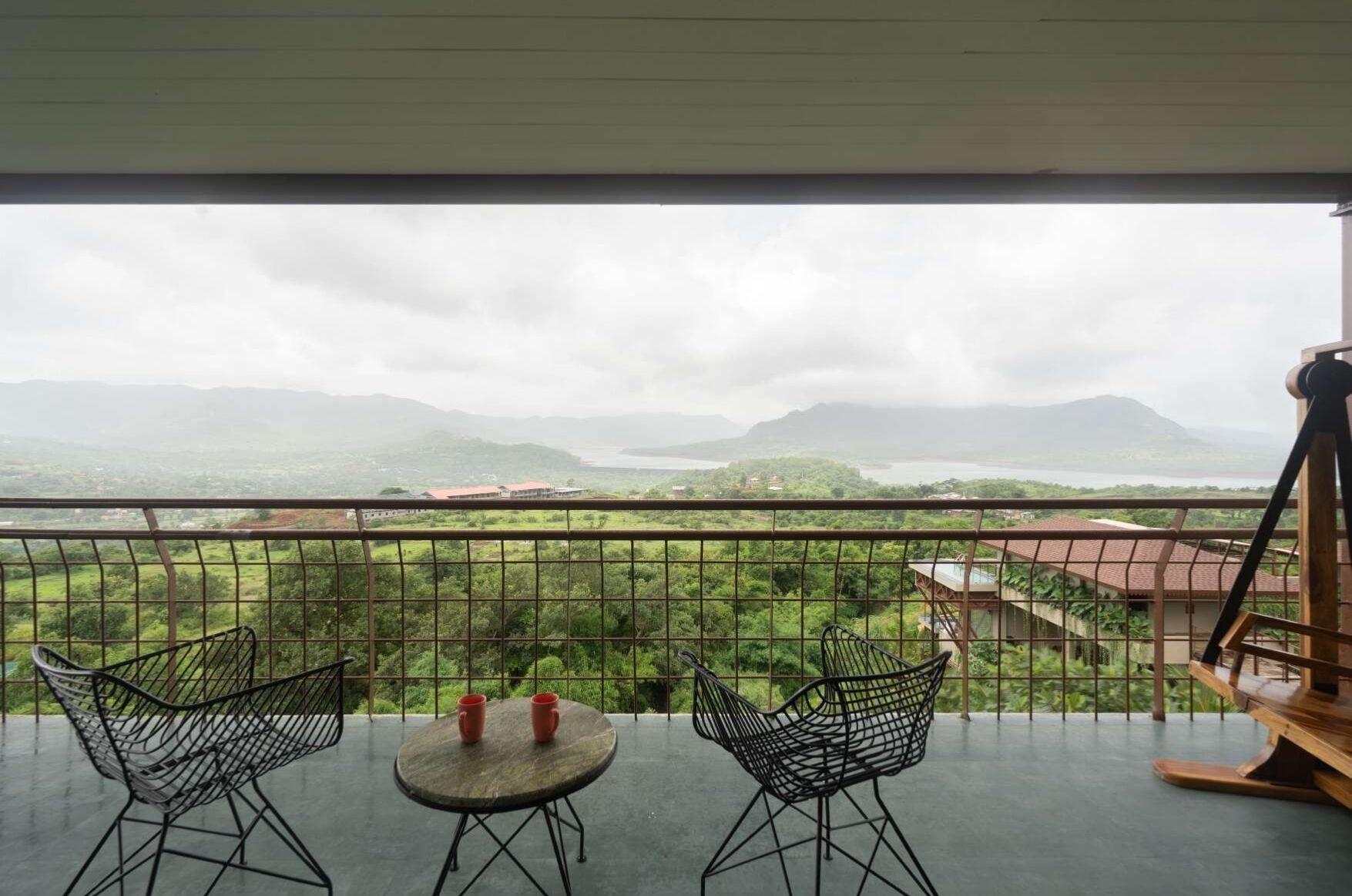 A balcony with two chairs and a table, overlooking a scenic landscape with mountains and a body of water.