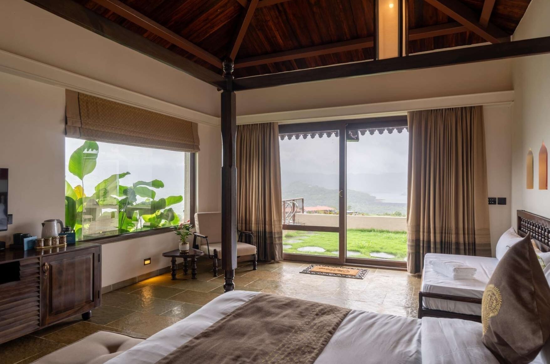 Une chambre spacieuse avec un grand lit, un bureau et une chaise, une fenêtre donnant sur l’extérieur et une porte-fenêtre coulissante qui mène à un balcon.