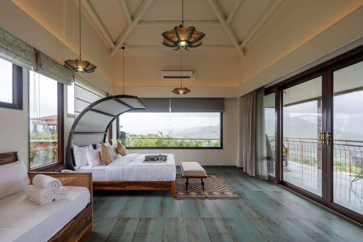A bedroom with a large bed, a sofa, a bench, and a view of the outdoors.
