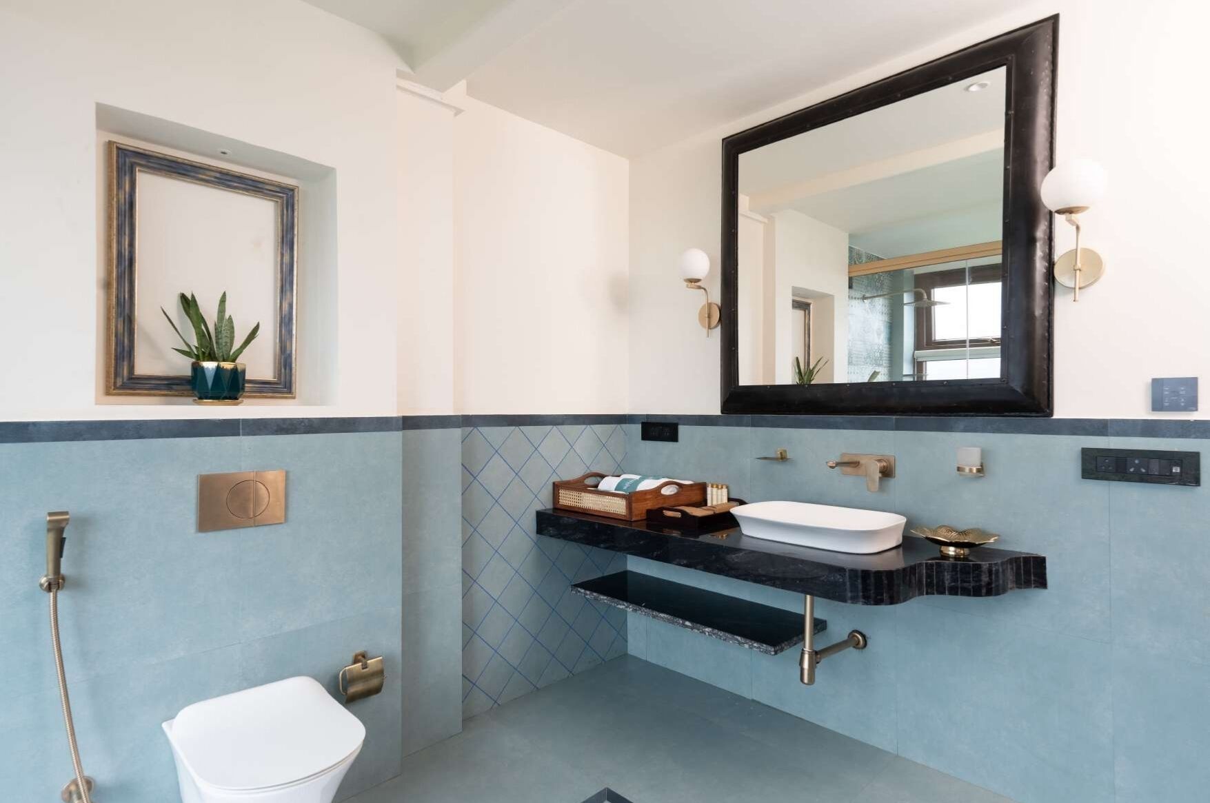 A bathroom with a white toilet, a sink with a black countertop, a mirror, and a wall-mounted shelf with toiletries.