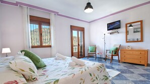A bedroom with a bed, two chairs, a dresser, a TV, and a balcony door. - A captivating retreat with pool for an exceptional group holiday. Pet friendly. (Comares)