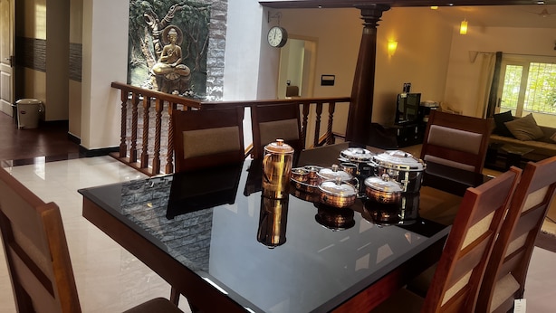 A dining area with a black table, wooden chairs, and a decorative Buddha statue on the wall. - Yercaud Bungalow Stay (Yercaud)