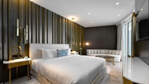 Una habitación de hotel moderna con una cama grande, un sofá, una mesita de noche con lámpara y un televisor.