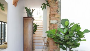 Una escalera con un arco de ladrillo, un armario de madera, una planta en maceta y un reposapiés de mimbre.
