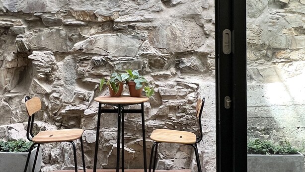 Un patio con un muro de piedra, una mesa de madera con dos sillas y plantas en macetas.