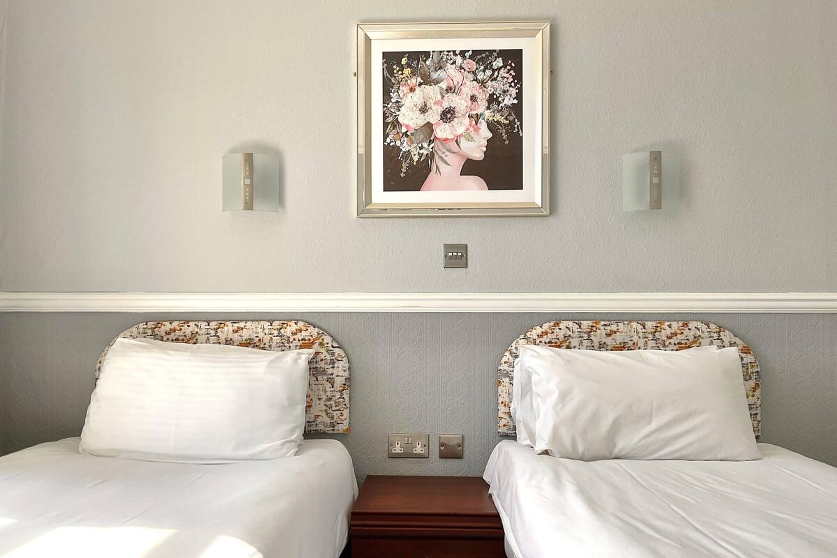 Ett hotellrum med två sängar, ett nattduksbord, en byrå och ett inramat blomstermotiv på väggen.