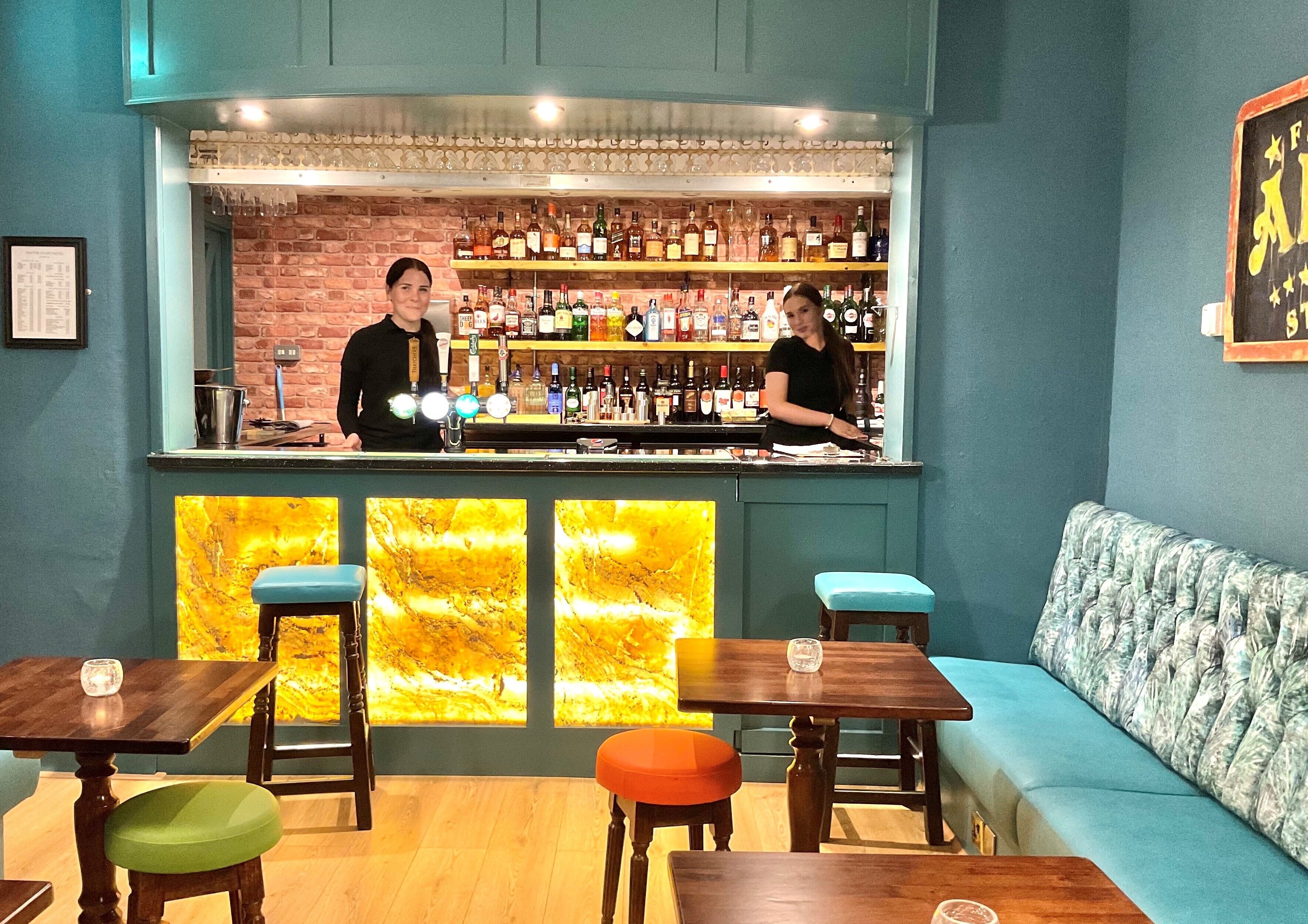 Un rincón de bar con pared de ladrillo, estantes llenos de botellas de licor y un sofá tapizado azul.