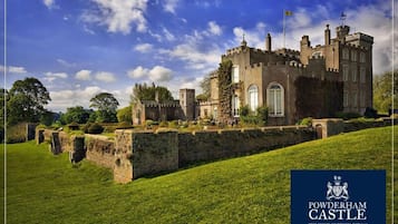 Castillo Powderham, con una imponente pared de piedra, una bandera y abundante vegetación.