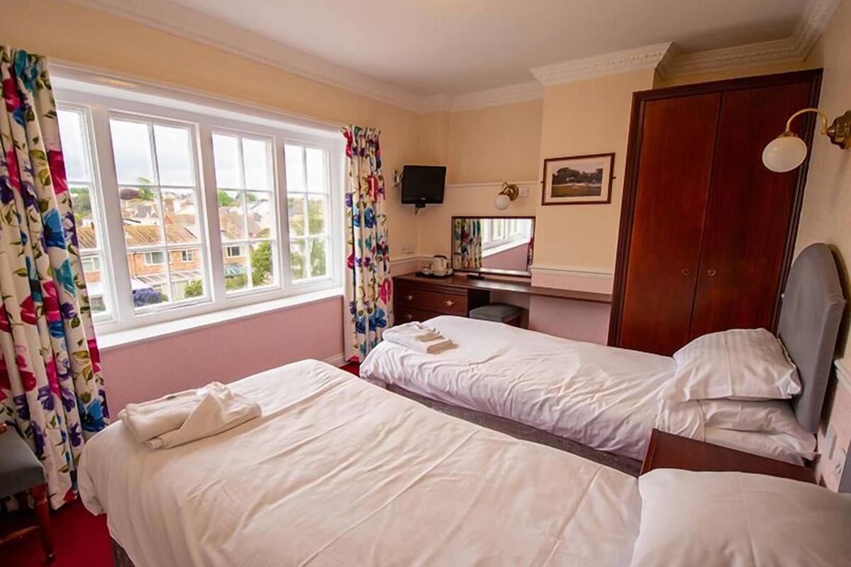 Ett hotellrum med två separata sängar, ett skrivbord med en tv, en garderob och ett fönster med gardiner.
