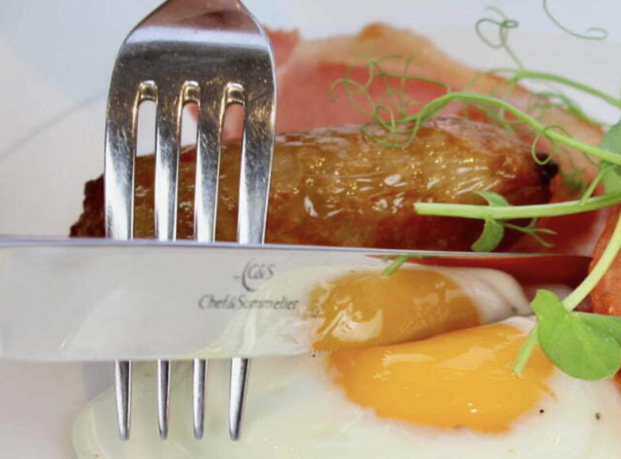 A fork holding a piece of food, a knife with a label, and a plate with a garnish.
