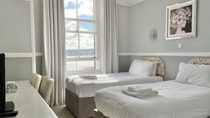 Una habitación de hotel con dos camas, un escritorio con silla, un televisor y una ventana con cortinas.