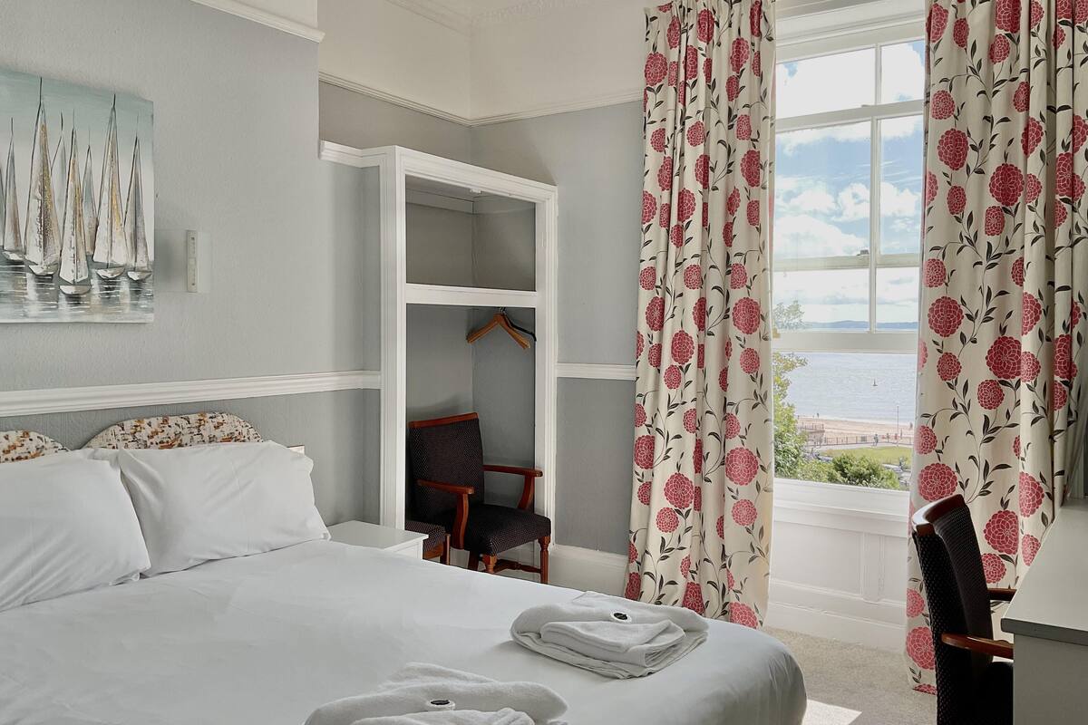 Ett hotellrum med en säng, en stol, en garderob och utsikt över havet.