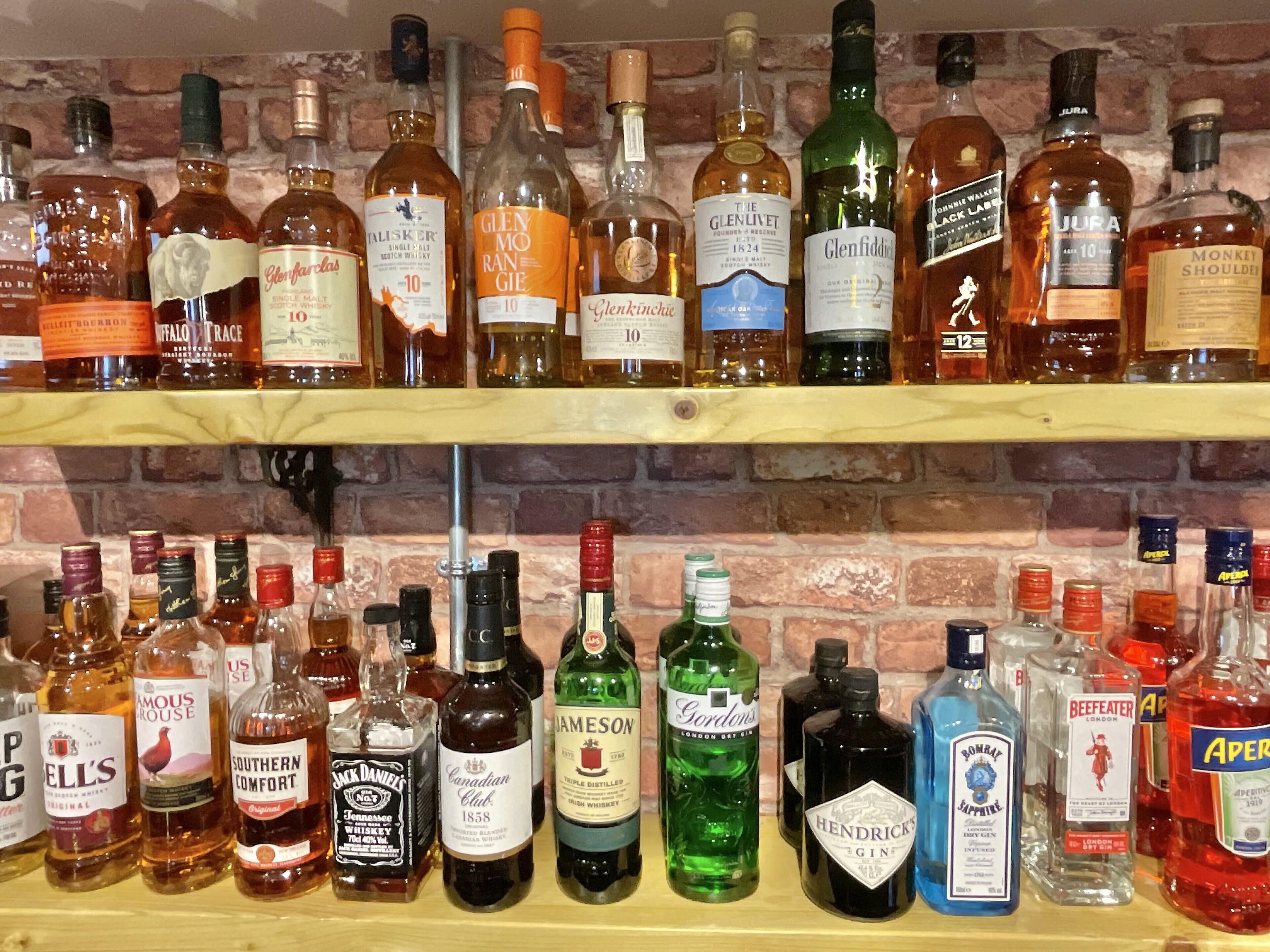 Two shelves of various liquor bottles against a brick wall.