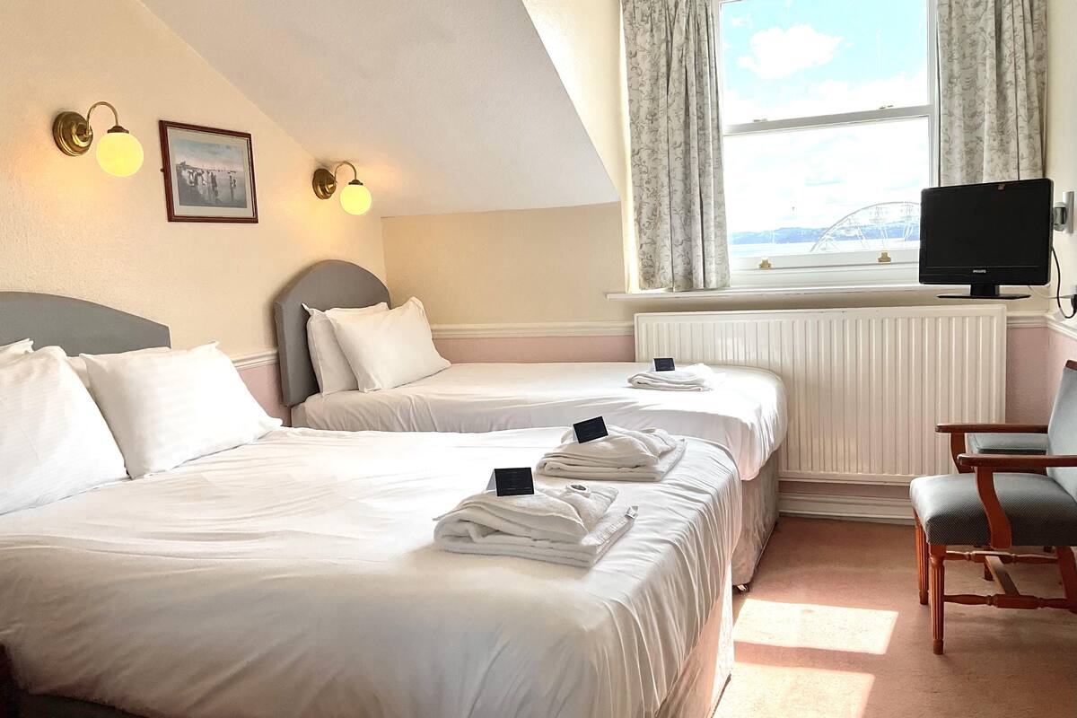 Ett hotellrum med två sängar, en tv, en stol och ett fönster med gardiner.