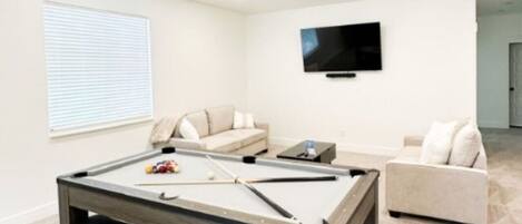 A pool table in a room with a ceiling fan, two sofas, and a TV mounted on the wall.