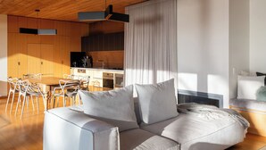 A modern living room with a wooden ceiling, a sofa with cushions, a dining area with chairs, and a kitchen in the background. - The Edge - an architecturally designed home with breathtaking views (Binalong Bay)