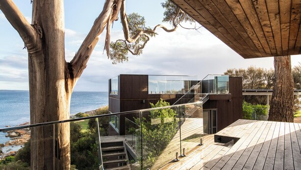 A modern wooden deck with glass railings overlooking a coastal landscape. - The Edge - an architecturally designed home with breathtaking views (Binalong Bay)