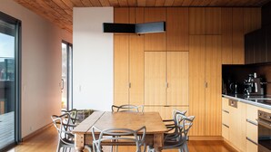 A modern kitchen with wooden cabinets, a central island with chairs, and a built-in oven. - The Edge - an architecturally designed home with breathtaking views (Binalong Bay)