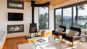 A modern living room with a fireplace, large windows, and a balcony with a view. - The Edge - an architecturally designed home with breathtaking views (Binalong Bay)