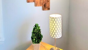 Un angolo di una stanza con pannello in legno, una piccola pianta in vaso, una lampada e un tavolino in legno.