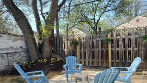 Un'area patio con sedie di plastica blu e un tavolino, circondata da una recinzione in legno e alberi.