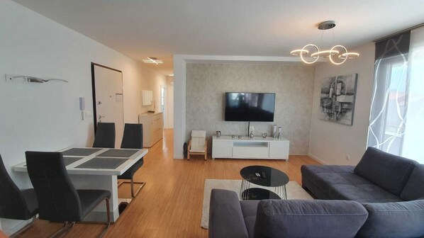 En moderne stue med et fladskærms-tv, en grå sofa, spisebord med stole og et hvidt tv-møbel.