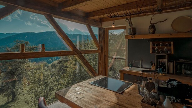 A rustic wooden interior with a large window overlooking a mountainous landscape.