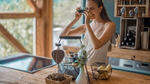 A woman taking a photo with a vintage camera in a rustic kitchen setting.