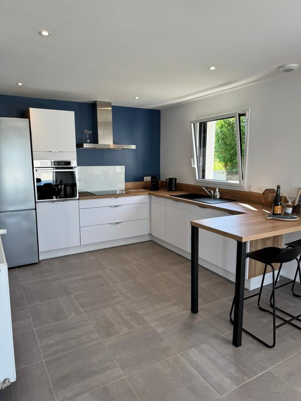 A modern kitchen with white cabinets, a stainless steel range hood, a built-in oven, a coffee maker, and a window providing natural light.