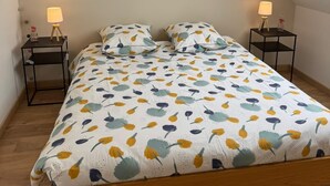 A bedroom with a sloped ceiling, a bed with a floral bedspread, two bedside tables with lamps, and a skylight. - The iodine parenthesis. House with garden - Near sea (Plozévet)