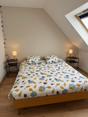 A bedroom with a sloped ceiling, a bed with a floral bedspread, two bedside tables with lamps, and a skylight.