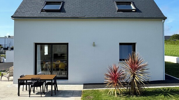 A modern house with a flat roof, two skylights, a large sliding glass door, and a small patio with a table and chairs. - The iodine parenthesis. House with garden - Near sea (Plozévet)