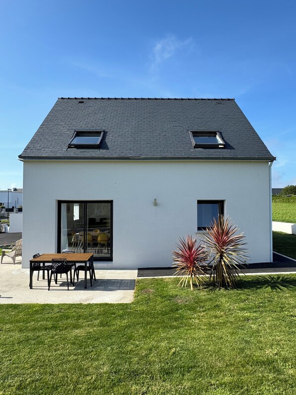 A modern house with a flat roof, two skylights, a large sliding glass door, and a small patio with a table and chairs.