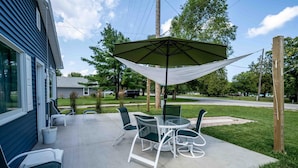 Une terrasse avec une table et des chaises, un auvent suspendu et une maison en arrière-plan.