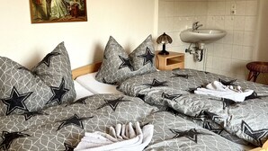 Una cama bien tendida con ropa de cama de diseño geométrico, una lámpara de noche, una mesita de noche de madera y un lavamanos fijado a la pared.