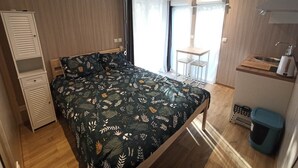A bedroom with a bed, a desk, a chair, a wardrobe, and a window with curtains.