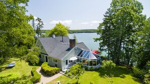 Une maison dotée d’une grande véranda en verre, d’une pelouse bien entretenue et offrant une vue sur un lac.