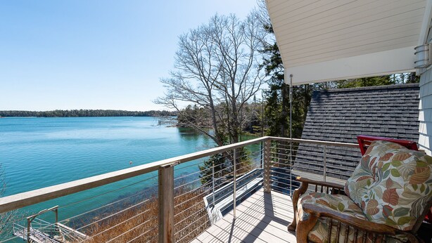 Un balcon donnant sur un lac, une terrasse en bois et une chaise agrémentée d’un coussin à motifs floraux.