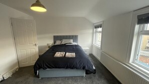 Relax in this serene bedroom with a large bed, a comfortable bench at its foot, and a convenient bedside table.