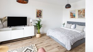 Ein modernes Schlafzimmer mit einem Bett, einem Fernseher, einer Topfpflanze und Kunstwerken an der Wand.