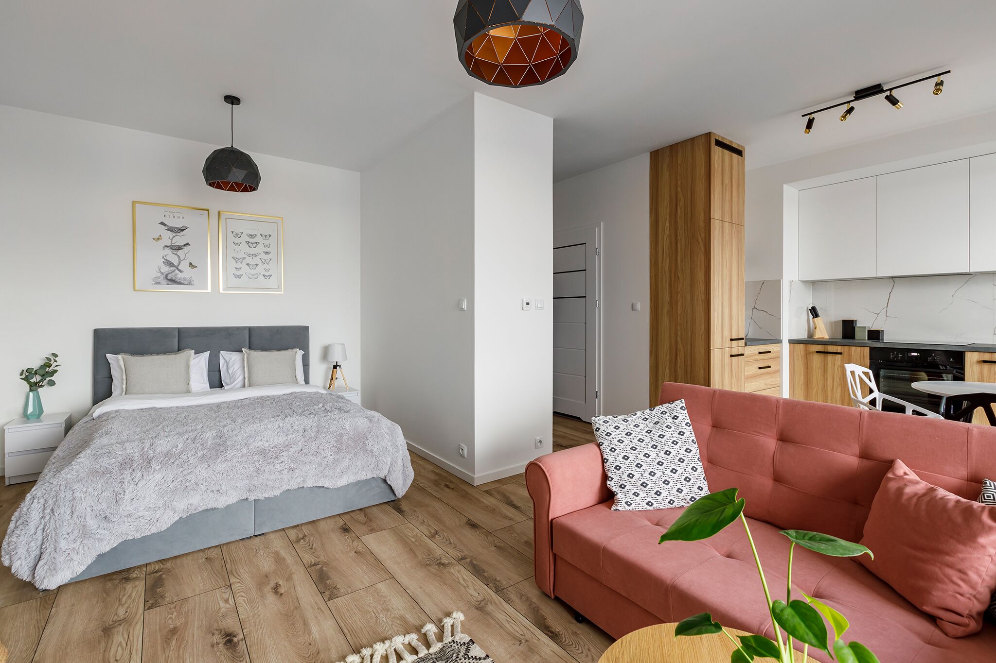 A modern bedroom with a large bed, a pink sofa, and a small kitchen area.