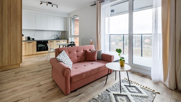Ein modernes Wohnzimmer mit einer Couch, einem kleinen runden Tisch und Blick auf die Küche sowie nach draußen.