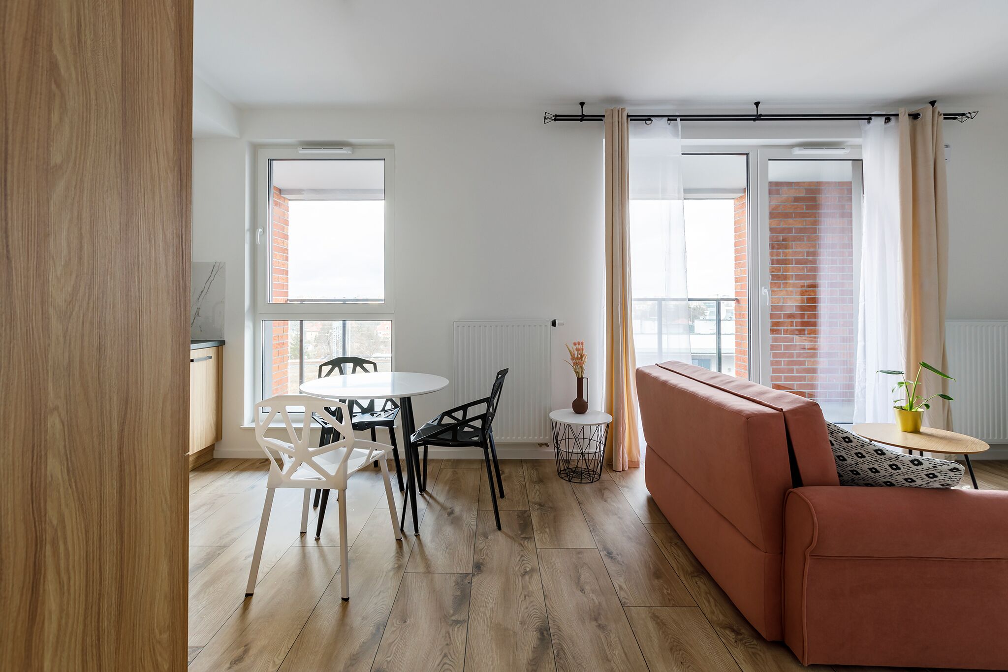 A modern living room with a sofa, a dining table with chairs, and a small side table with a plant.