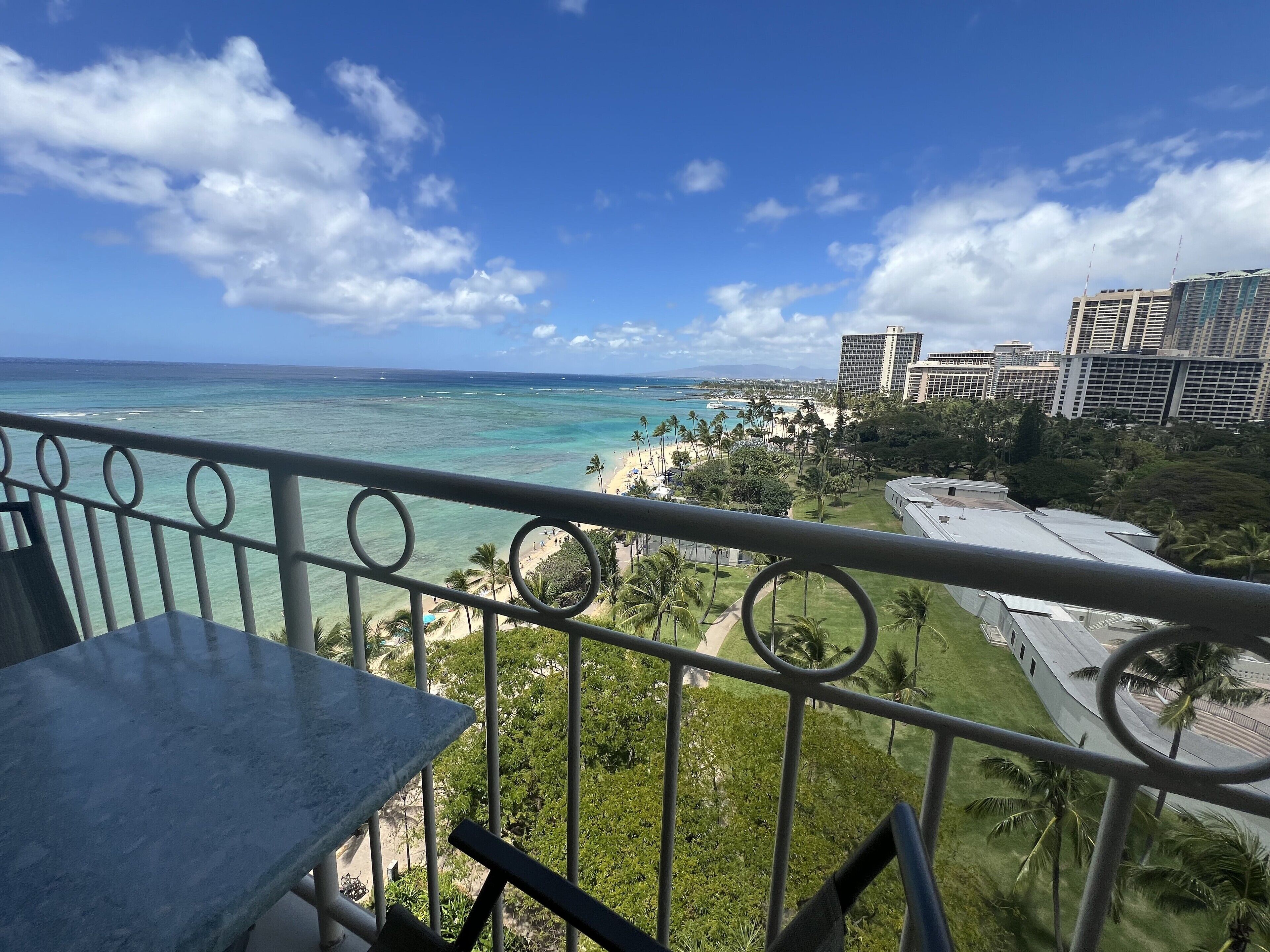 A balcony with a view of a beach, palm trees, and a cityscape.