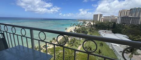 A balcony with a view of a beach, palm trees, and a cityscape.