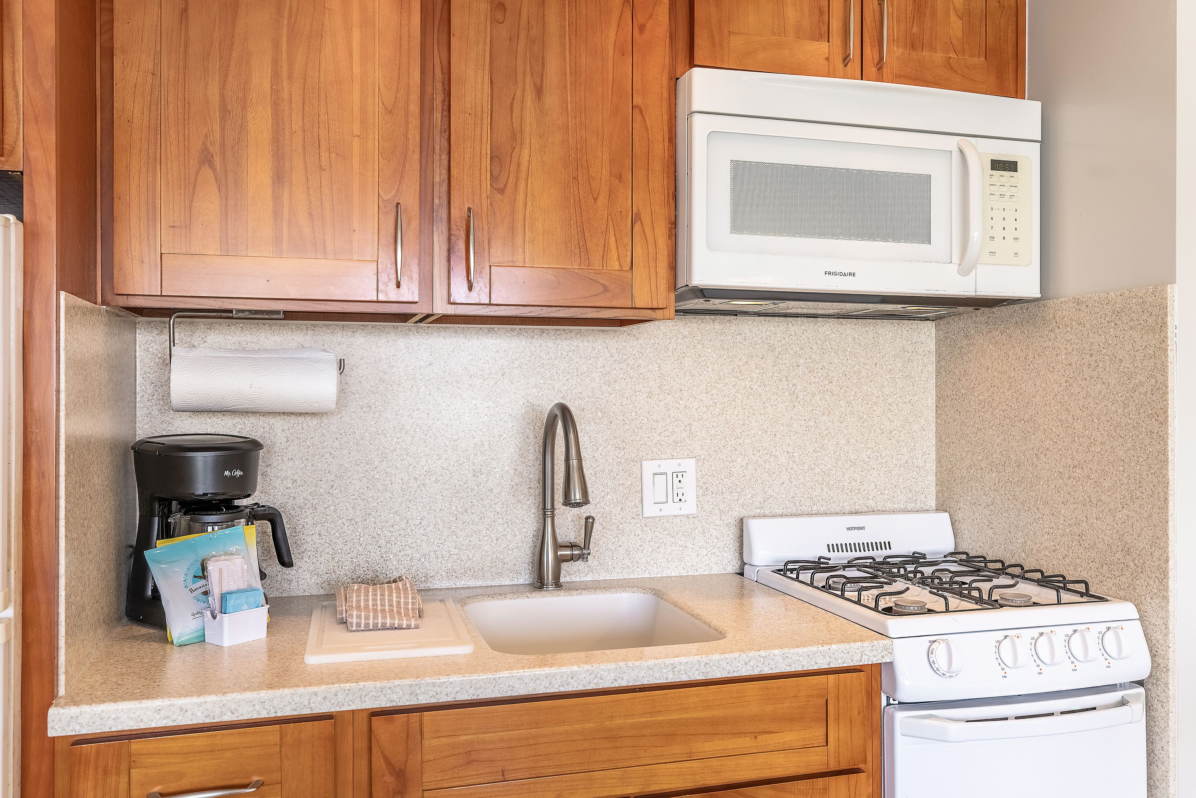 A kitchen with wooden cabinets, a white microwave, a gas stove, a coffee maker, and a countertop with a paper towel holder.