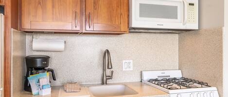 A kitchen with wooden cabinets, a white microwave, a gas stove, a coffee maker, and a countertop with a paper towel holder.