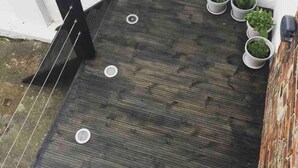 A small outdoor area with a dark wooden floor, three white circular objects, and several potted plants against a white wall. - Stunning 2-bed Pet Friendly Apartment in Gateshead (Gateshead)